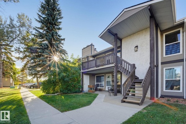 Townhouse exterior with a paved walkway leading to units. Mature trees are visible on the left. - 1180 Saddleback Rd Nw, Edmonton