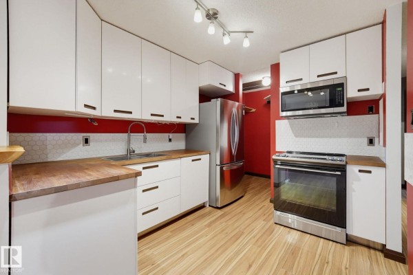 Kitchen with white cabinetry, stainless steel appliances, butcher block countertops, and red tile backsplash. - 1180 Saddleback Rd Nw, Edmonton