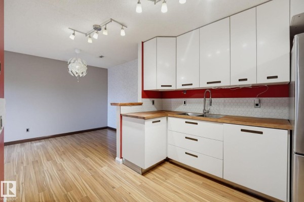 Kitchen and dining area with white cabinetry, butcher block counters, and a modern chandelier. - 1180 Saddleback Rd Nw, Edmonton