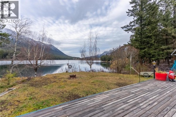 Wooden deck with outdoor furniture and planters overlooks a lake surrounded by trees and mountains. - 11805 Fountain Valley Road, Lillooet