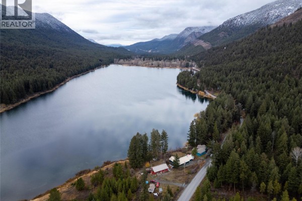 Aerial view of a property with multiple buildings nestled among pine trees on the shore of a lake. - 11805 Fountain Valley Road, Lillooet