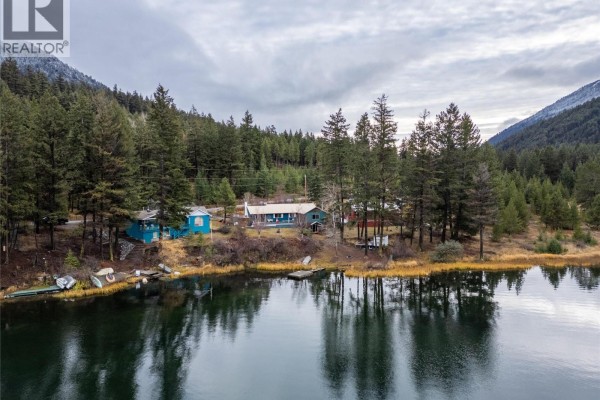 Several buildings on the edge of a lake surrounded by dense forest and snow-dusted mountains. - 11805 Fountain Valley Road, Lillooet