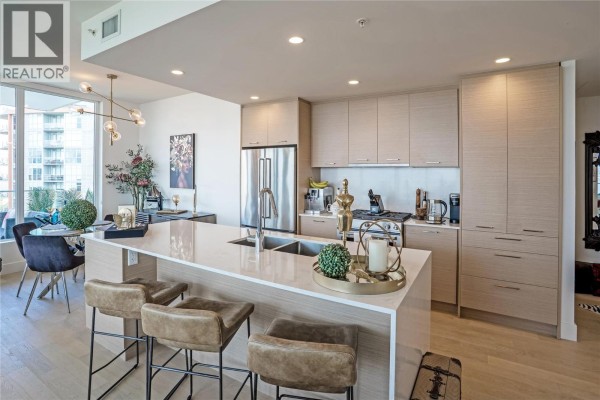 Modern kitchen with a large island, waterfall countertop, stainless steel appliances, and light wood cabinets. - 1181 Sunset Drive Unit# 1405, Kelowna