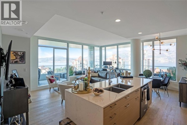 Open-concept living and dining area with large windows, city and lake views, and a kitchen island. - 1181 Sunset Drive Unit# 1405, Kelowna