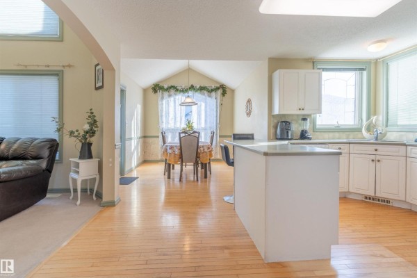 Kitchen with white cabinets, granite countertops, and a breakfast bar, adjacent to a dining area. - 11813 12 Av Nw, Edmonton