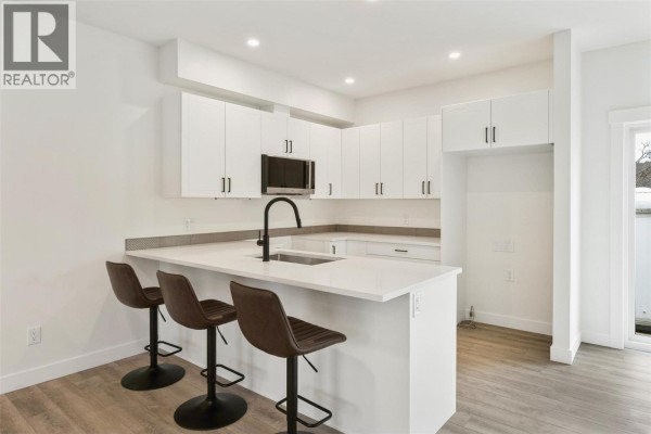 Modern kitchen with white cabinets, quartz countertop, and bar seating - 11815 Grant Avenue Unit# 102, Summerland