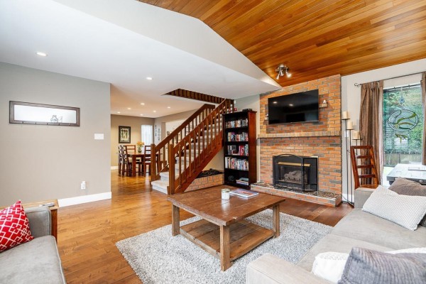 Living room with a fireplace, wood-paneled ceiling, staircase, and a view into the dining area. - 11826 Alderwood Crescent, Delta
