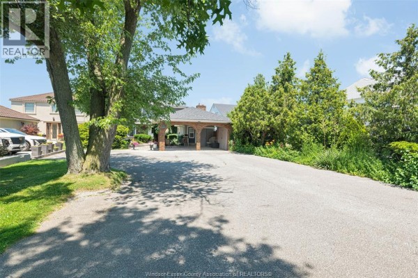 Asphalt driveway curves towards a brick carport attached to a house. - 11830 Riverside Drive East, Windsor