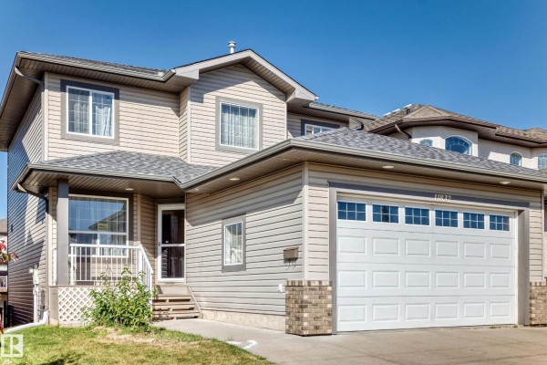 Side exterior view of a two-story house with beige siding, a gray roof, and attached garage. - 11832 173 Av Nw, Edmonton