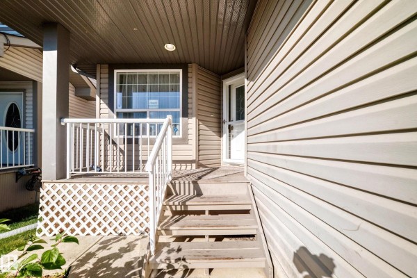 View of the front porch with wooden stairs, white railing, and beige siding. - 11832 173 Av Nw, Edmonton