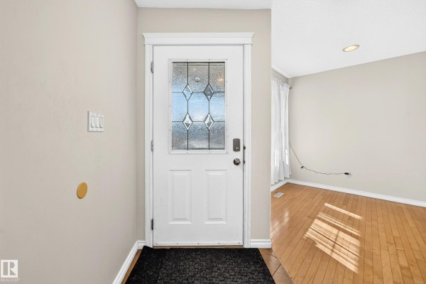 Interior view of the front entrance with a white door with glass panels and light wood flooring. - 11832 173 Av Nw, Edmonton