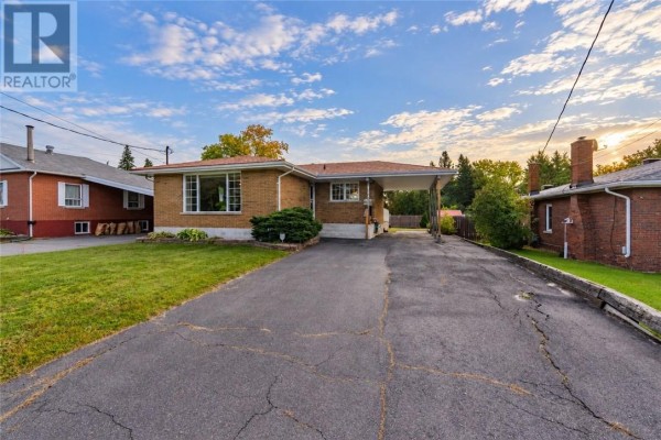 Front view of a brick bungalow with a carport and paved driveway on a sunny day. - 1184 Drummond Street, Sudbury
