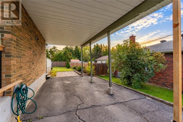 Covered carport area next to the brick house, leading to a paved driveway and backyard. - 1184 Drummond Street, Sudbury