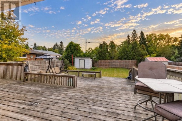 Wooden deck with patio furniture overlooking a fenced backyard with a swing set and shed. - 1184 Drummond Street, Sudbury