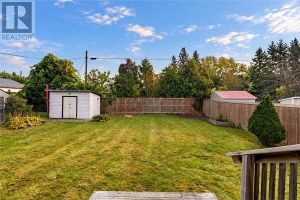 View of a green backyard with two sheds, a wooden fence, and mature trees. - 1184 Drummond Street, Sudbury