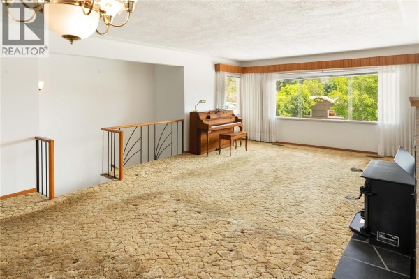 Living room with beige carpet, a wood piano, and a large window with green trees outside. - 1188&1190 Hartwick Street, Kelowna