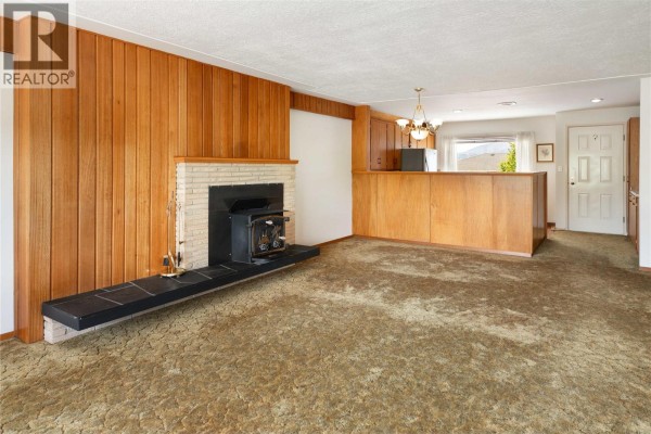 Living room featuring a fireplace, wood paneling, a kitchen counter, and a view of the backyard. - 1188&1190 Hartwick Street, Kelowna