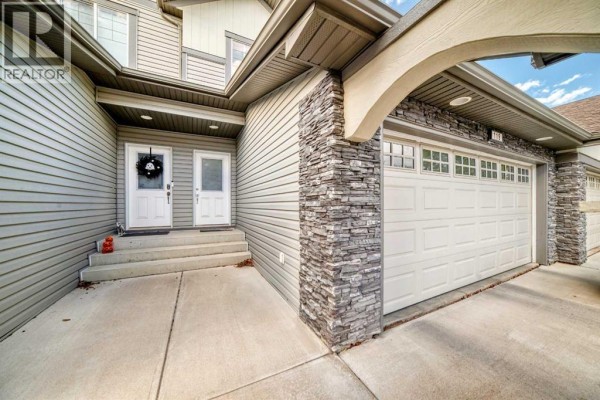 Close-up of the townhouse entrance with two doors, a garage door, and stone accents. - 119, 100 Coopers Common Sw, Airdrie