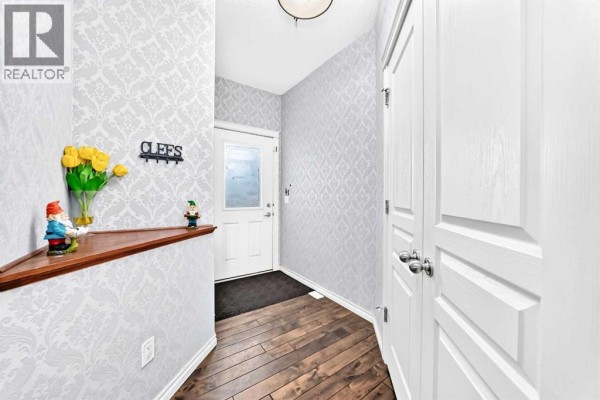 Interior entryway with patterned wallpaper, wood floors, and a corner shelf with decor. - 119, 100 Coopers Common Sw, Airdrie