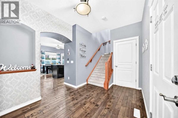 Hallway view showing wood floors, grey walls, a staircase, and an archway to another room. - 119, 100 Coopers Common Sw, Airdrie