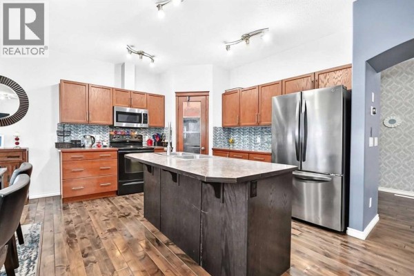 Kitchen with wood cabinets, stainless steel appliances, a large island, and wood plank flooring. - 119, 100 Coopers Common Sw, Airdrie