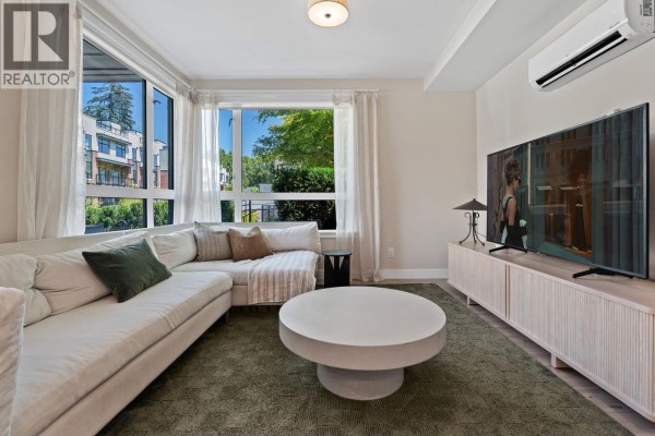 Living room with a sectional sofa, television, and large windows overlooking greenery. - 119 2035 Glenaire Drive, North Vancouver