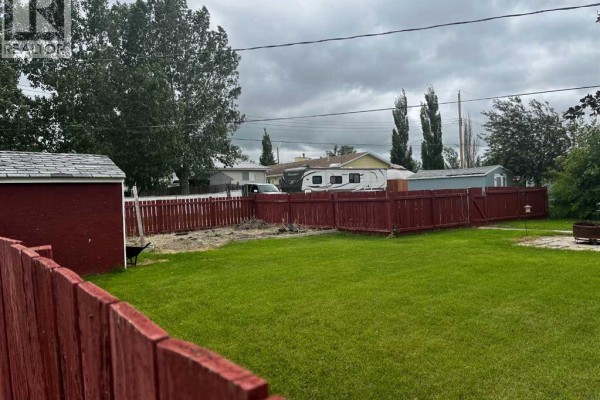 View of a brick building with tall evergreen trees and a residential property nearby. - 119 3 Avenue W, Hussar