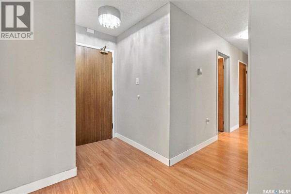 Interior view of a closed wooden apartment door with a patterned rug on the floor. - 119 3410 Park Street, Regina