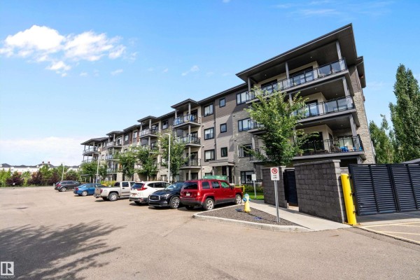 View of the apartment building's side facade with balconies and a parking lot in front. - #119 524 Griesbach Pr Nw Nw, Edmonton