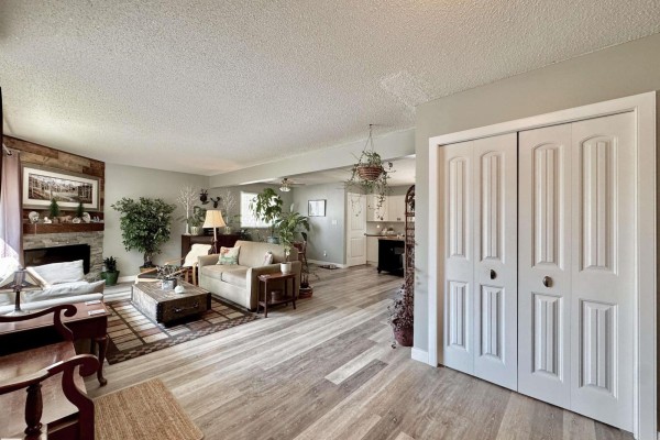 Open-concept living area with a fireplace, sofa, coffee table, and kitchen in the background. - 119 Garland Cr, Sherwood Park