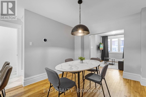 Dining area and open doorway to living room with grey sofa and window. - 119 Hopewell Avenue, Ottawa