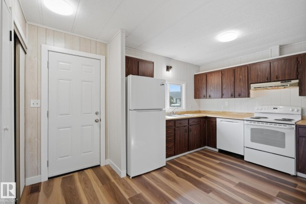 Kitchen with white appliances, dark wood cabinets, and a white door leading to the exterior. - 119 Parkland Acres, Lacombe