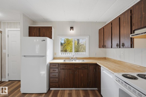 Kitchen corner view with white appliances, dark wood cabinets, and a sink overlooking the yard. - 119 Parkland Acres, Lacombe