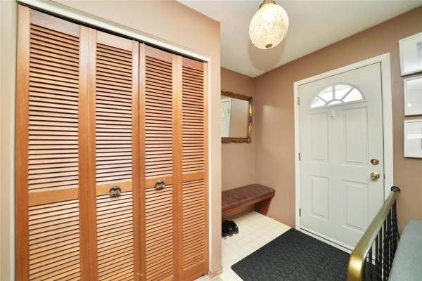 Interior entrance hall with double wood louvered doors, white front door, and bench. - 119 Sanderson Avenue, Winnipeg
