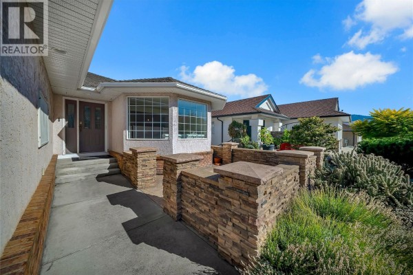 View of a house entrance with a covered walkway, double doors, and a low stone wall with plants. - 11907 Quail Ridge Place, Osoyoos