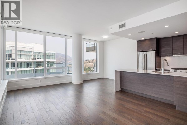 Kitchen with dark wood cabinetry, stainless steel appliances, and a waterfall island in an open-concept living space. - 1191 Sunset Drive Unit# 2905, Kelowna