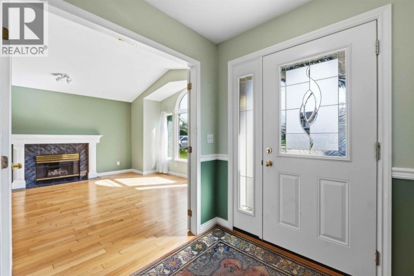 View from the entryway into the living room, featuring a fireplace and large windows with light curtains. - 11915 238a Street, Maple Ridge