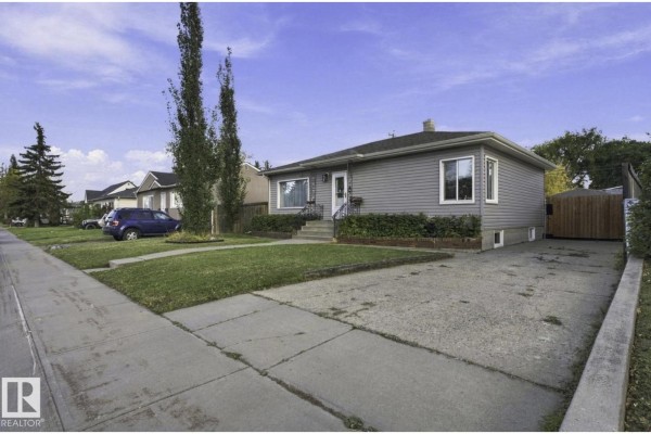 Side view of a light grey bungalow with a long concrete driveway leading to a detached garage. - 11928 127 St Nw, Edmonton