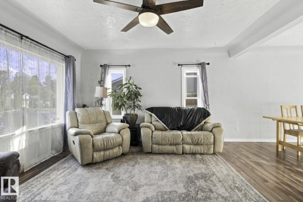 Living room with beige reclining chairs, a sofa, large rug, wood laminate flooring, and large windows. - 11928 127 St Nw, Edmonton