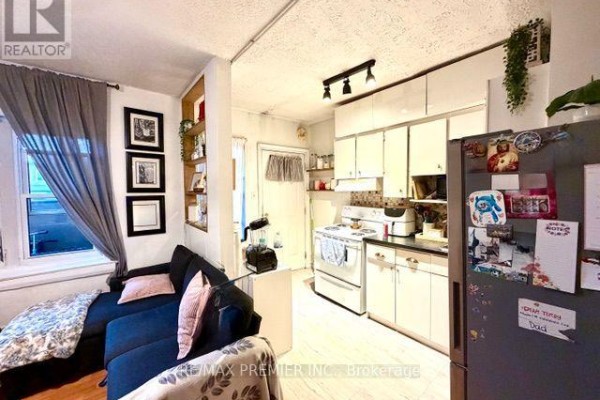 Living area with a dark blue sectional sofa, entertainment unit with a television, and a dining table. - 1193 St Clair Avenue W, Toronto