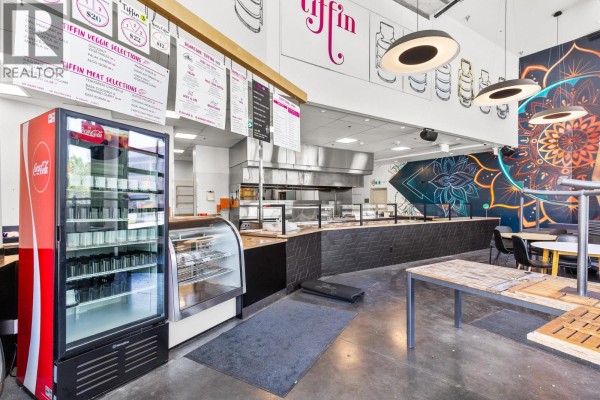 Commercial kitchen and serving area with stainless steel equipment, display cases, and a colorful mural. - 1193 Sunset Drive, Kelowna