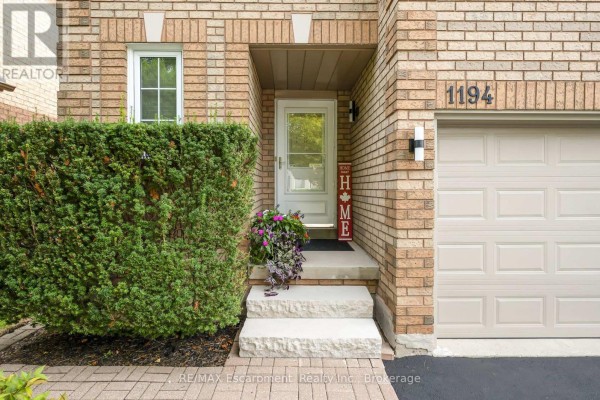 Close-up of the front entrance with a white door, stone steps, and green hedges. - 1194 Old Oak Drive, Oakville