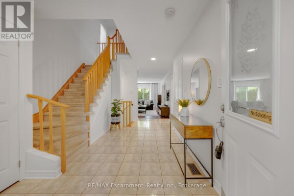 Interior foyer with beige tile floor, beige walls, and a wooden staircase. - 1194 Old Oak Drive, Oakville