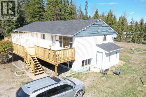 Side view of a white duplex home featuring a large wooden deck and stairs. - 1195-1197 Omega Road, Quesnel