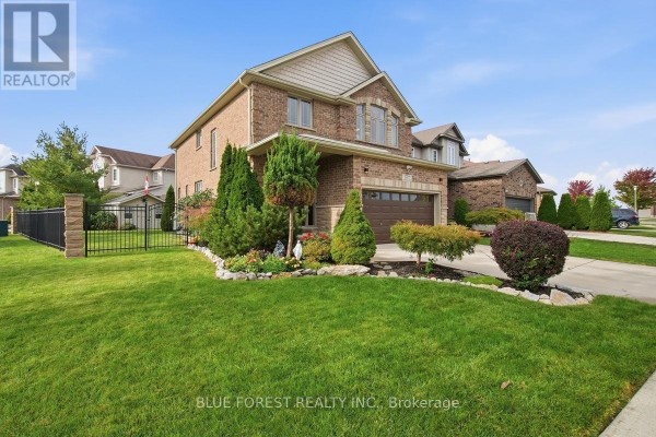 Side view of a brick house with manicured lawn, shrubs, and a black metal fence. - 1197 Cardinal Road, London South