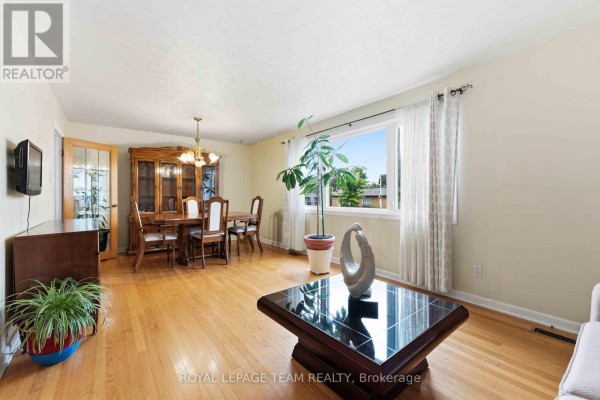 Living and dining room with hardwood floors, large window, and wooden furniture. - 1197 Maitland Avenue, Ottawa