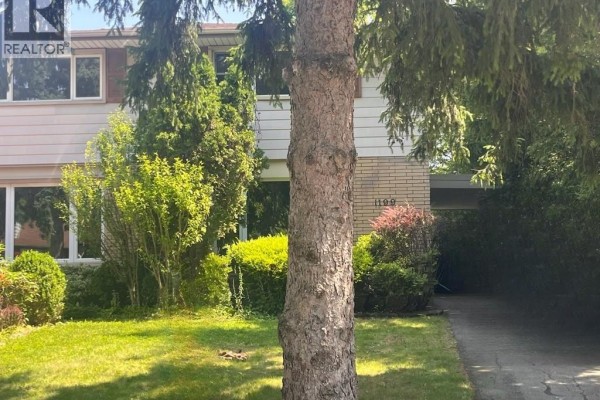 Front view of a house with beige siding, brick accents, and a tree in the foreground. - 1199 Nottingham Avenue, Burlington