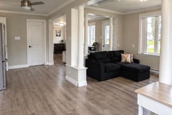 Living room with a dark sectional sofa, beige walls, and light wood-look flooring. - 1199 Route 133 Road, Grand Barachois