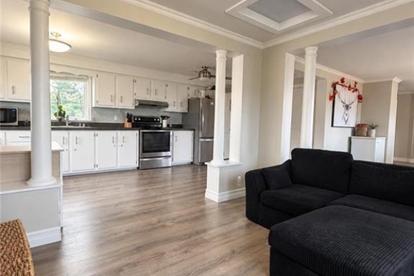 Open concept living area and kitchen with white cabinets, stainless steel appliances, and gray flooring. - 1199 Route 133 Road, Grand Barachois