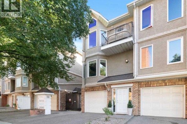 Exterior of a townhouse with brick lower level, beige stucco upper level, balconies, and garage doors. - 12, 1339 14 Avenue Sw, Calgary